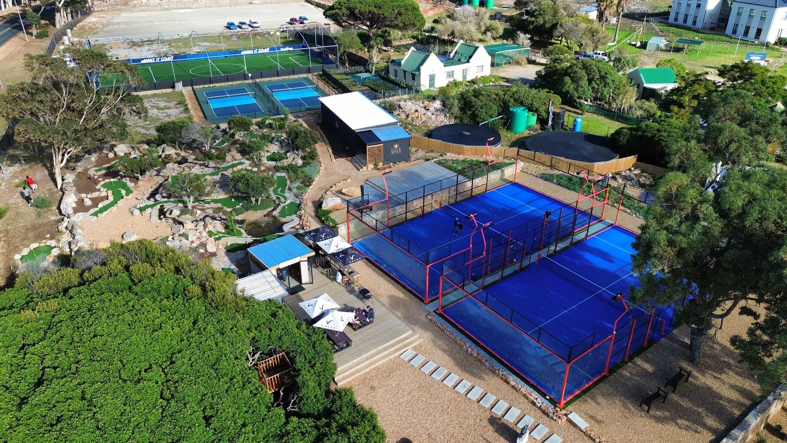 Volea from above: two padel courts in play, the putt-putt course, the pickleball courts and the 5-a-side pitch, set among trees at Imhoff Farm.